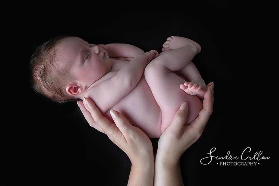 Sleeping baby in mother's hands by newborn photographer Sandra Cullen